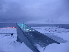 people are standing in the snow near a large structure with lights on it's sides