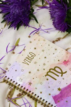 an open notebook sitting on top of a table next to purple flowers