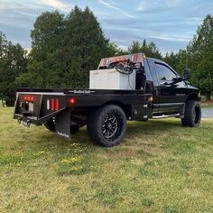 the truck is parked on the grass by the water in the field with trees behind it