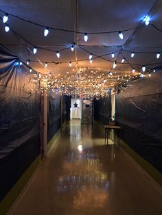 a long hallway with lights strung from the ceiling and on to the walls, in front of a blue tarp