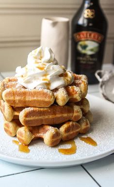 a stack of waffles topped with whipped cream and syrup on a white plate