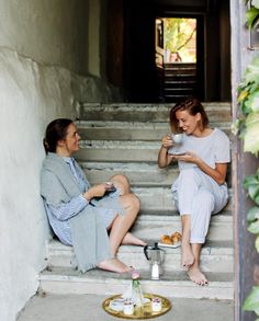 two women sitting on the steps drinking coffee and talking to each other while having tea