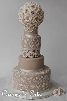 a three tiered wedding cake with white flowers on the top and bottom layer is decorated in lace