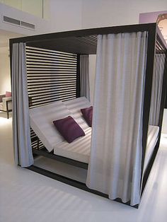 a bed that is in the middle of a room with curtains on both sides and pillows on the bottom