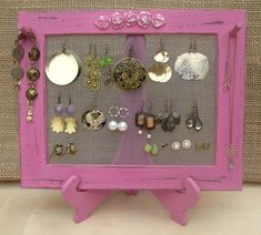 there is a pink frame with many different earrings on it and a few other things hanging from the wall