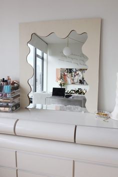 a mirror sitting on top of a white dresser next to a desk with a laptop