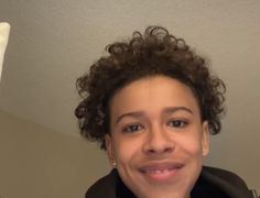 a close up of a person wearing a jacket and smiling at the camera with curly hair