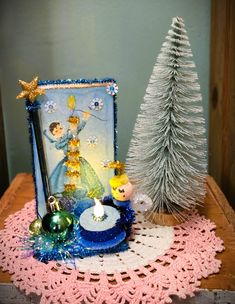 a small christmas tree next to a card and some ornaments on a doily table