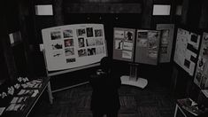 a black and white photo of a person looking at pictures on display in a dark room