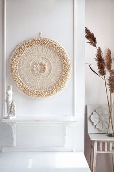 a white table with some vases and plants on it next to a wall hanging