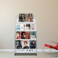 a magazine rack with magazines on it next to a red chair