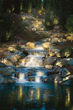 there is a small waterfall in the middle of some rocks and water with lights on it