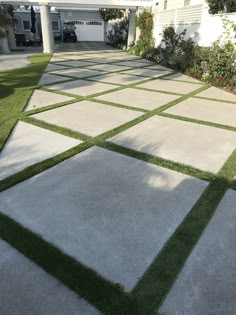 an outdoor area with grass and concrete tiles on the ground in front of a house