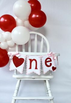 a baby's first birthday chair with balloons and one sign hanging from the back