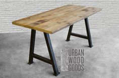 a wooden table sitting on top of a cement floor next to a brick wall with the words urban wood goods written below it