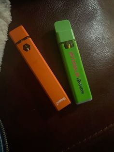 two lighters sitting next to each other on top of a leather surface, one green and the other orange