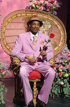 a man in a pink suit and hat sitting on a chair with a flower bouquet