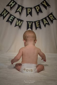 a baby in diapers sitting on a bed with a happy new year banner above it