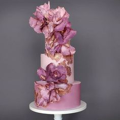 a three tiered cake with pink flowers on top and gold leaf decorations around the edges