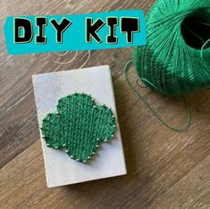 a green piece of yarn sitting on top of a wooden table next to a ball of thread