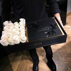 a man holding a black box with white roses in it and some glasses on top