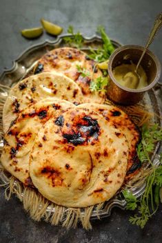 three flat breads on a metal plate with some sauce and herbs next to it