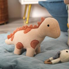 a crocheted toy dinosaur laying on a bed next to a stuffed animal