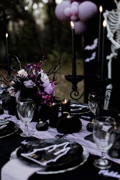 the table is set with black and white plates, silverware, purple flowers and candles