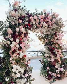 an outdoor wedding ceremony with flowers and greenery on the side of the aisle, overlooking the water