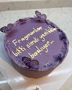 a birthday cake with purple frosting and butterflies on the top is sitting on a table