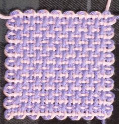 a close up view of a purple and white woven object on a black cloth with a needle