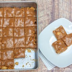 a pan filled with peanut butter squares on top of a wooden table next to a white plate