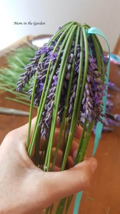 a person holding some purple flowers in their hand on a wooden table with blue ribbon