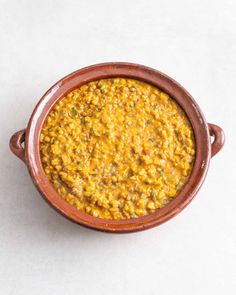 a brown bowl filled with yellow food on top of a white table