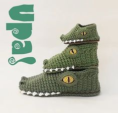 two crocheted crocodile shoes with yellow eyes and white feet are shown in front of a green sign that says alligator