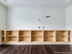 an empty room with wooden shelves and hard wood flooring on the far wall is a white painted wall