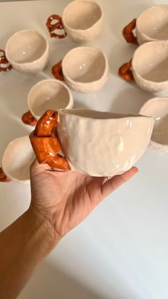 a hand holding a white bowl in front of many small bowls on a table top