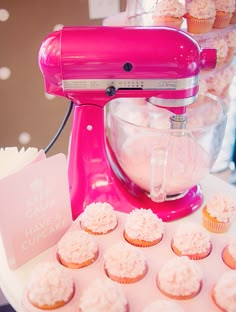 cupcakes are being made in front of a pink mixer on a table with other cupcakes