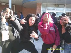 four young people posing for the camera in front of a building with their hands up