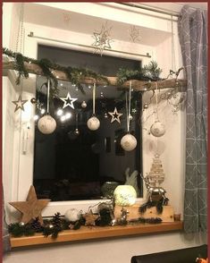 a window with ornaments hanging from it's side and a christmas tree on the other side