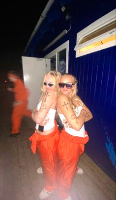 two women in orange pants and white shirts with tattoos on their arms are standing next to each other