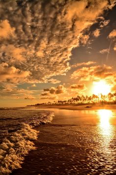 the sun is setting at the beach with waves coming in to shore and clouds above