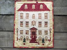 a quilted wall hanging on the side of a wooden fence with a red and white house