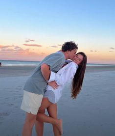 a man and woman kissing on the beach at sunset with people in the distance behind them