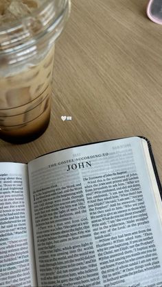 an open book sitting on top of a wooden table next to a cup of coffee