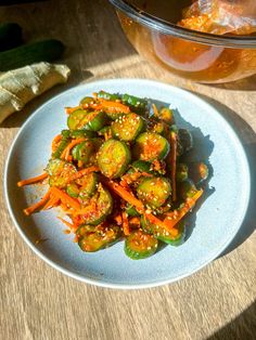 a white plate topped with carrots and cucumbers next to a bowl of pickles