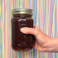 a hand holding a jar of chocolate jam in front of a multicolored wall