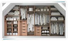 an attic closet with lots of white clothes and linens on shelves, under the slanted roof