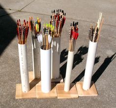 several white vases with different types of arrows in them on a wooden stand outside