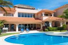 a large house with a pool in front of it and palm trees around the pool